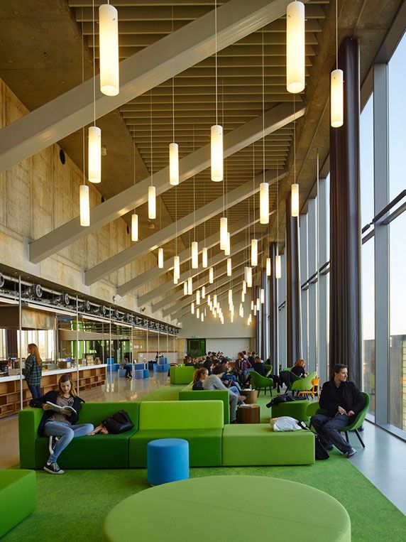 people are sitting in the lobby of an office building with green furniture and large windows