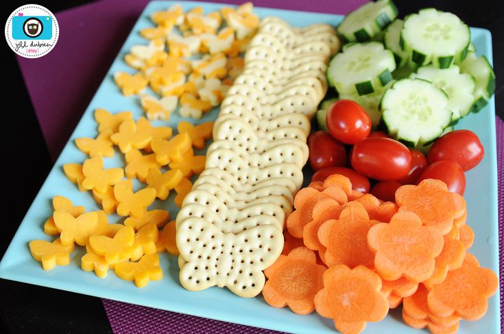 a blue plate topped with crackers and veggies next to cucumbers