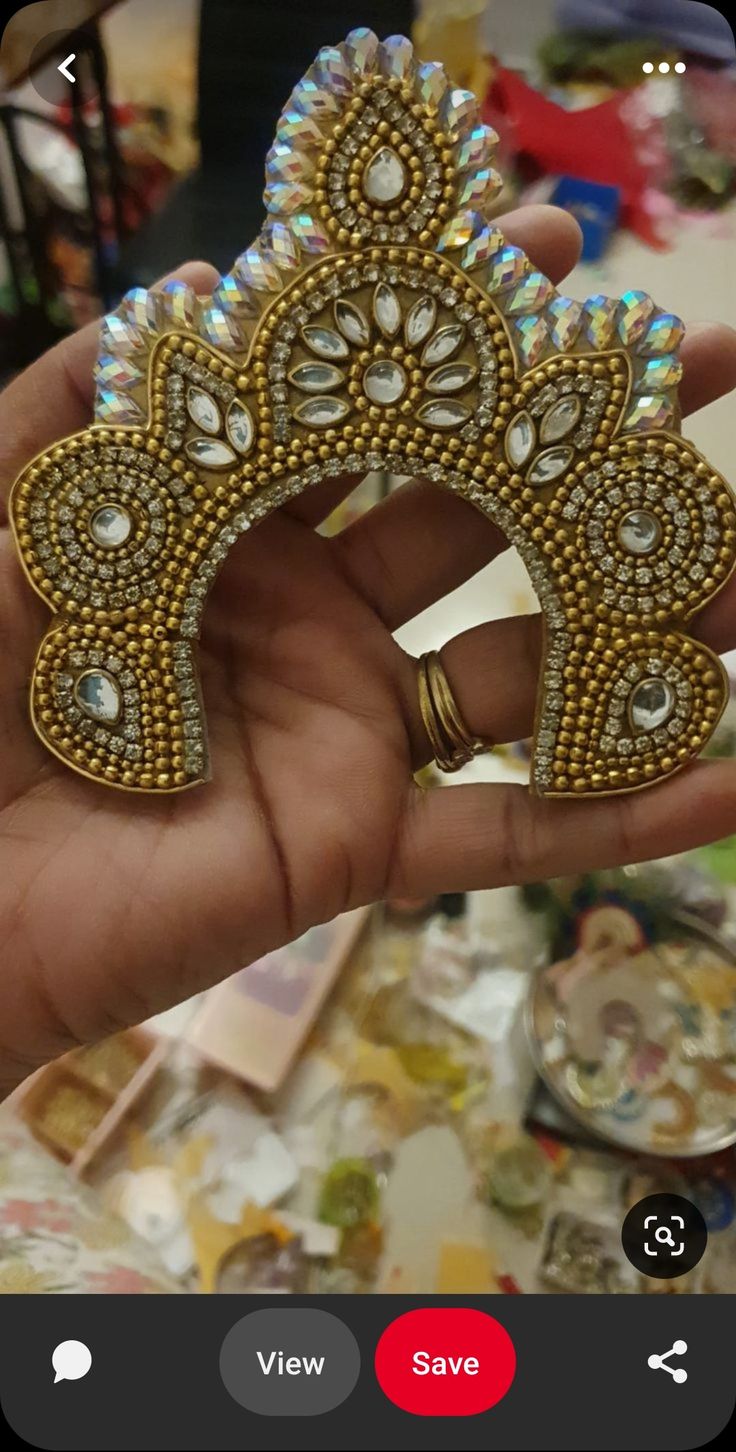 a hand holding a gold and white brooch in it's right hand, with other items on the table behind it