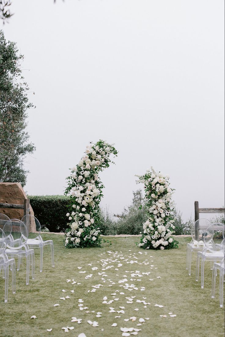 an outdoor ceremony with white flowers and clear chairs