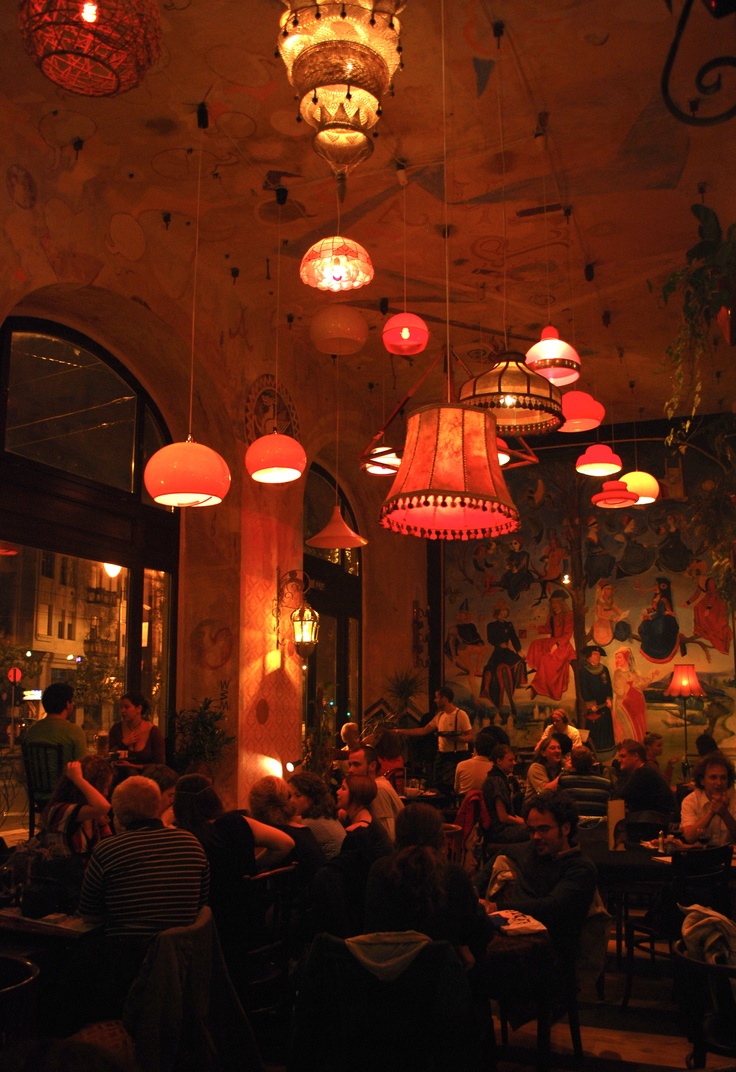 people sitting at tables in a restaurant with lights hanging from the ceiling