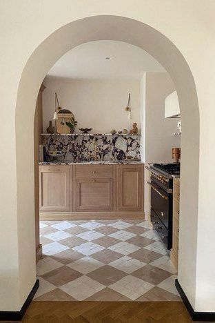 an archway leading into a kitchen with tile flooring and wooden cabinets on either side