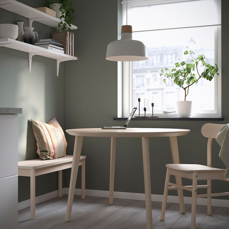 a small table and two chairs in a room with green walls, potted plants on the window sill