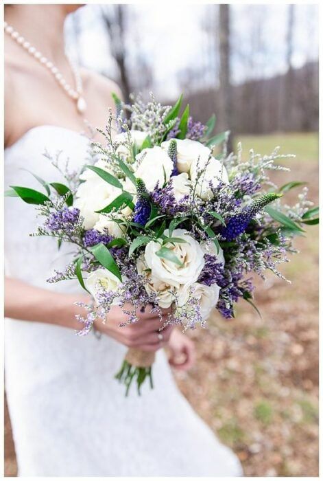 a bride holding a bouquet of white and purple flowers