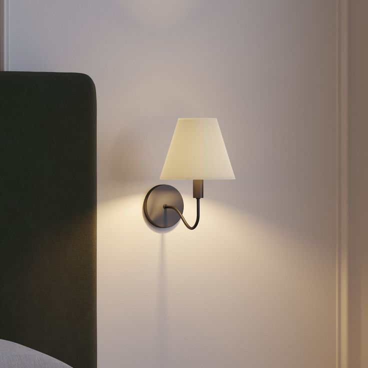 a lamp on the wall next to a bed in a room with white walls and black headboard