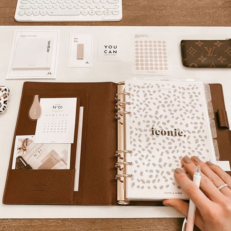 a woman's hand is holding an open notebook on top of a desk with various office supplies