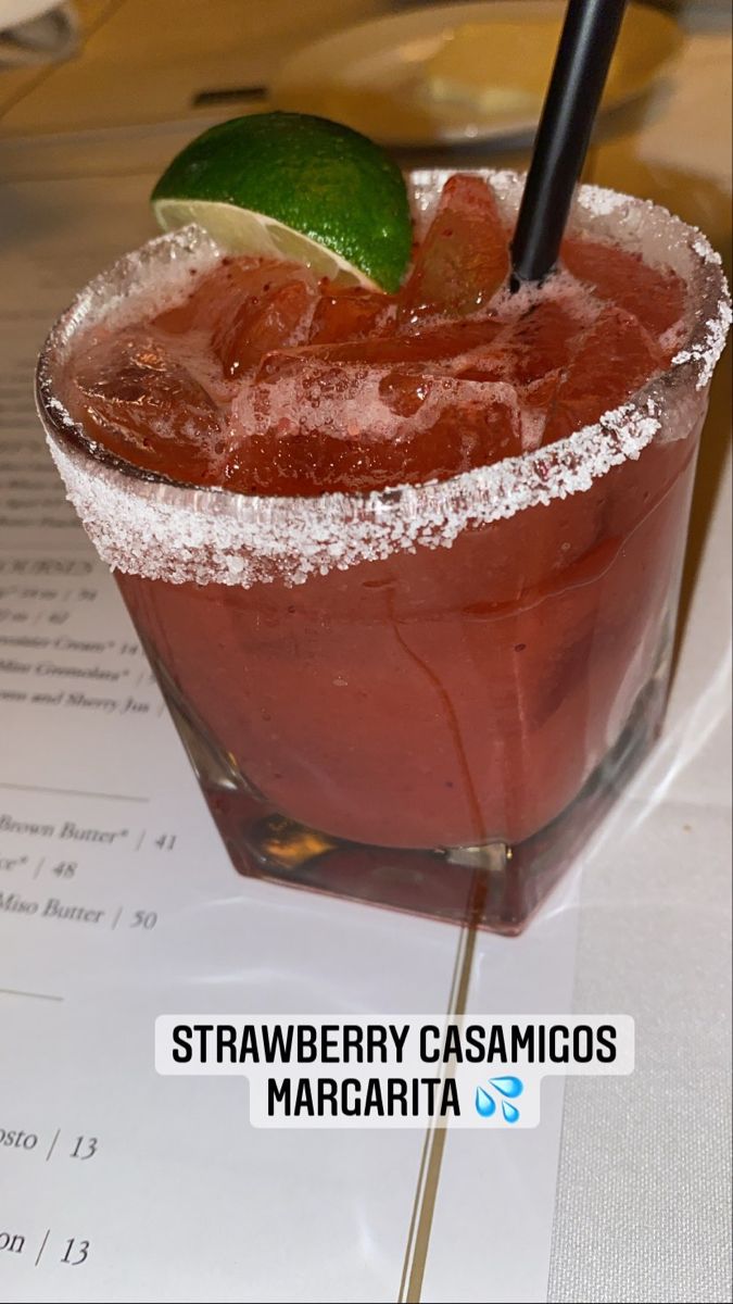 a red drink sitting on top of a table next to a paper with a lime