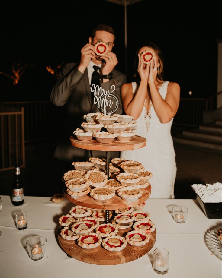 a man and woman standing next to each other in front of a table filled with pies