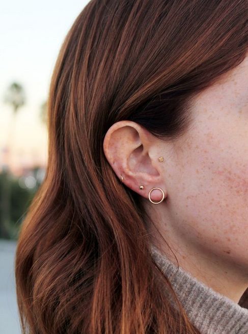 a woman with freckled hair is wearing gold earring and looking off into the distance