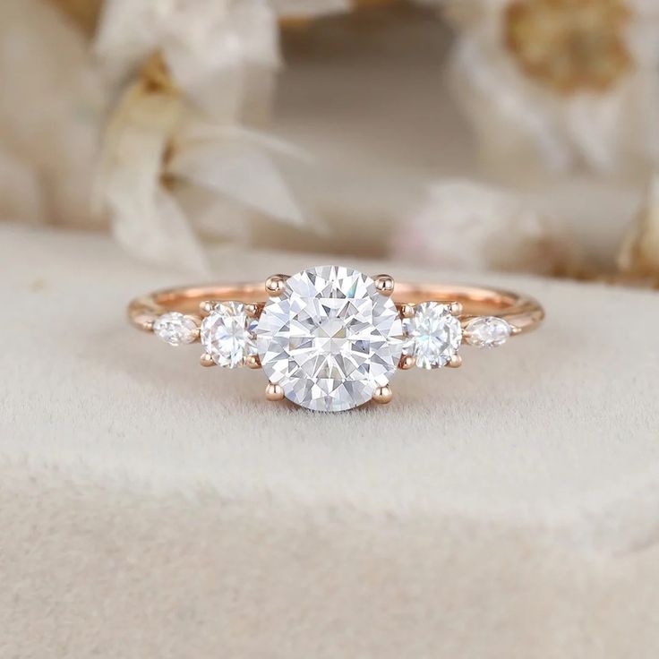 an engagement ring with three stones on top and flowers in the background, sitting on a white cloth