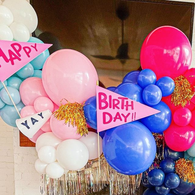 balloons and streamers in front of a birthday party sign on a fireplace mantel