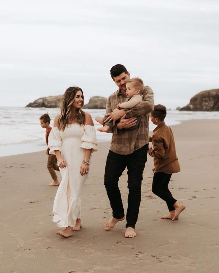 a man and woman holding a baby on the beach with other people in the background