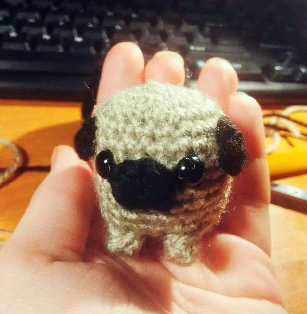 a small crocheted animal is held in front of a keyboard