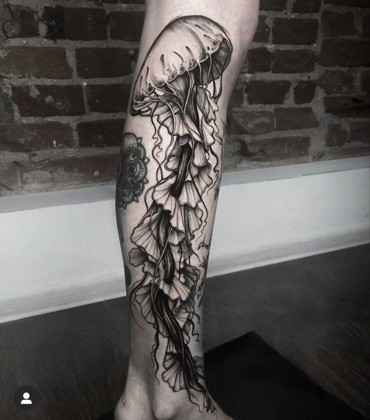 a black and white photo of a jellyfish tattoo on the right leg with flowers