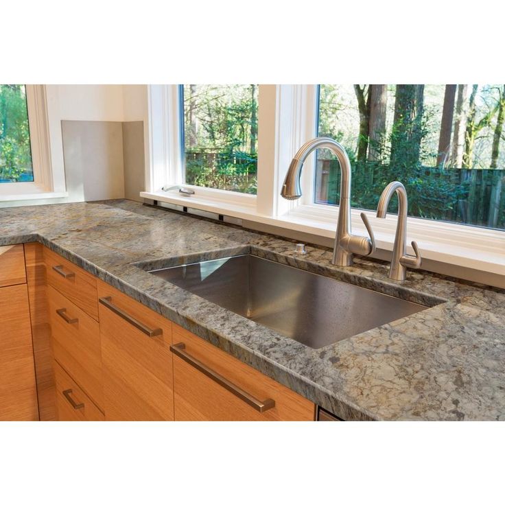 a kitchen with granite counter tops and wooden cabinets in front of two large windows that look out onto the woods