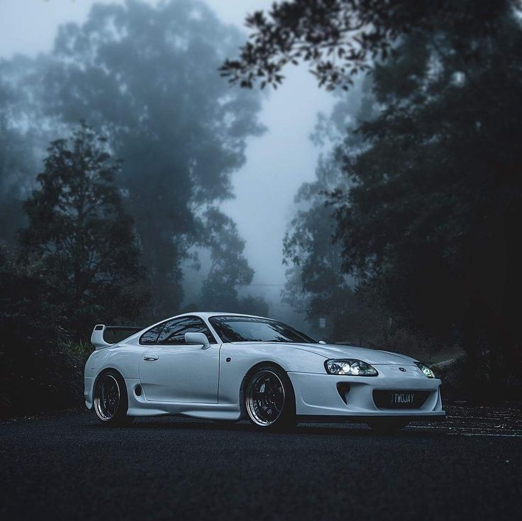 a white sports car parked on the side of a road in front of some trees