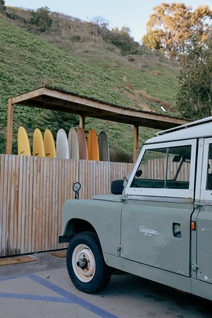 a van parked in front of a wooden fence with surfboards behind it