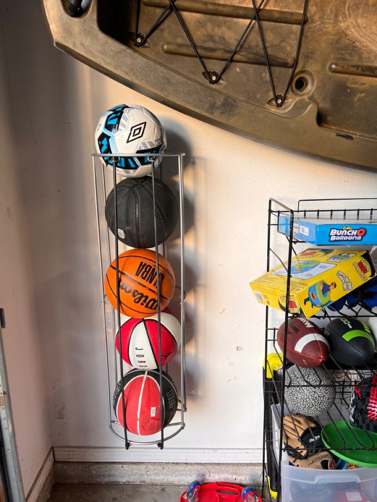 several sports balls and helmets are hanging on a rack in the corner of a room