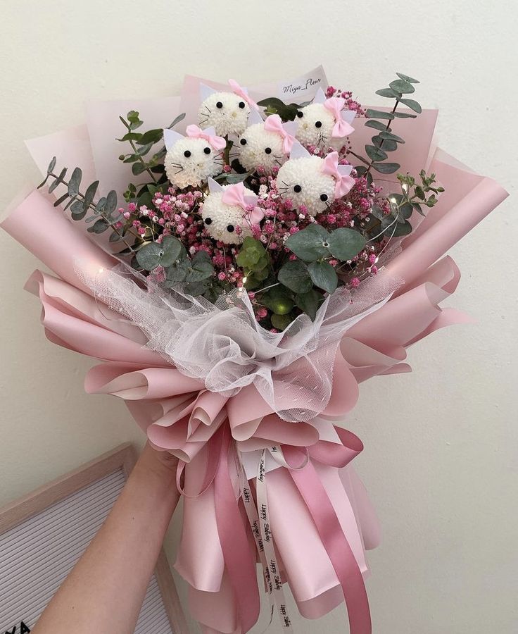 a bouquet of pink and white flowers is held by a woman's hand in front of a wall