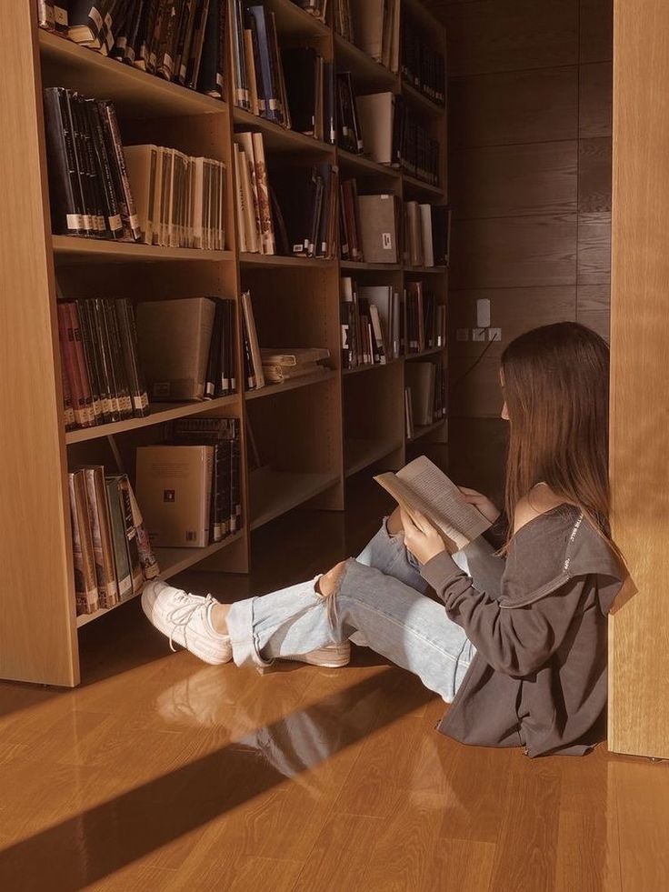 a woman sitting on the floor reading a book in front of a bookshelf