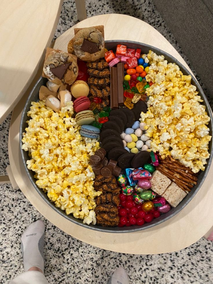 a bowl filled with candy and candies on top of a wooden table next to someone's feet