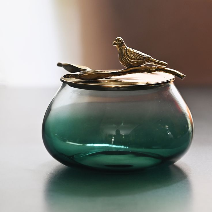 a glass vase with a bird sitting on it's top and the lid is empty