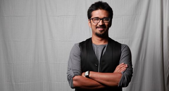 a man standing with his arms crossed in front of a white backdrop and wearing glasses