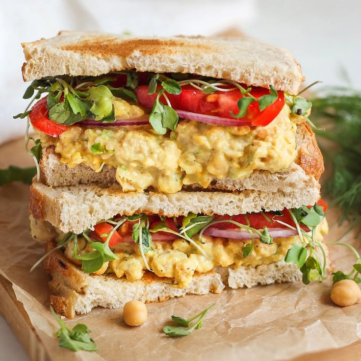 an egg salad sandwich with tomatoes, lettuce and chickpeas on toasted bread