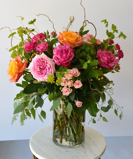 a vase filled with pink and orange flowers on top of a white marble table next to a wall