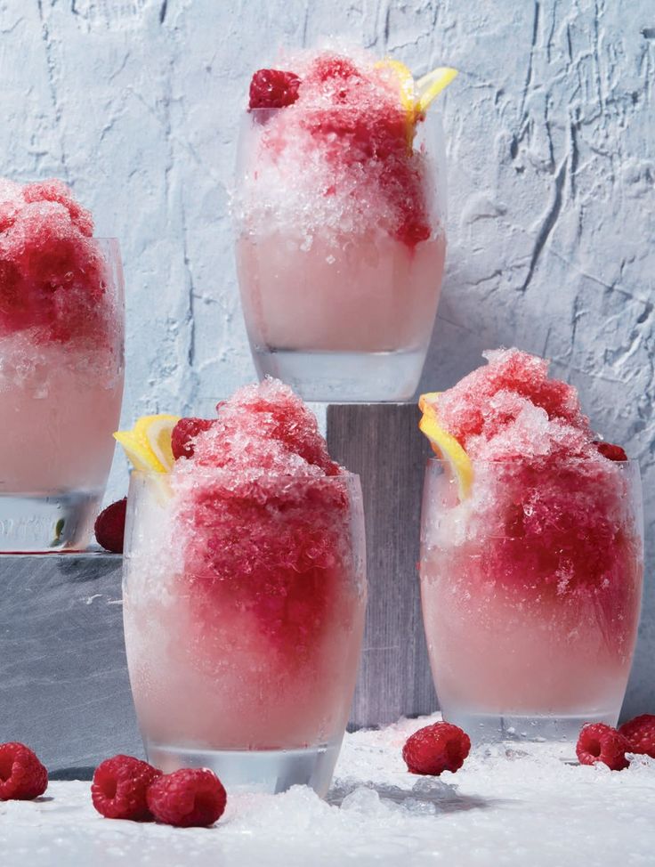 four glasses filled with ice and raspberries sitting on top of snow covered ground