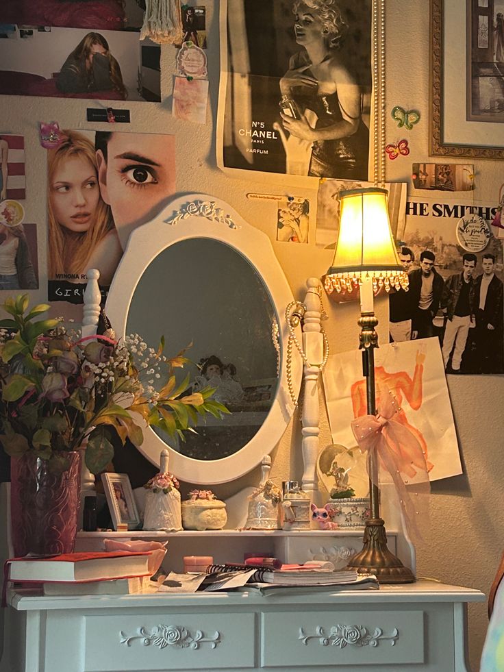 a white dresser topped with a mirror next to a wall covered in pictures and flowers