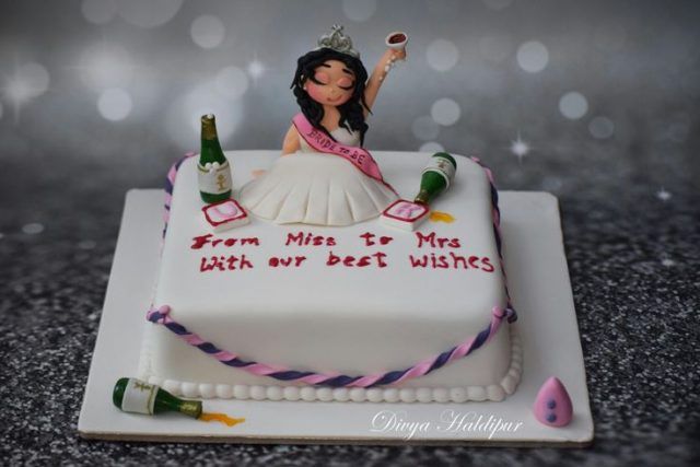 a cake decorated with a woman holding a bottle and two wine bottles on top of it