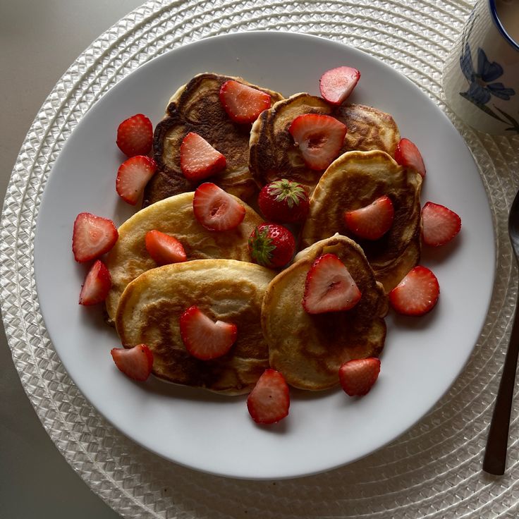 a white plate topped with pancakes covered in strawberries next to a cup of coffee