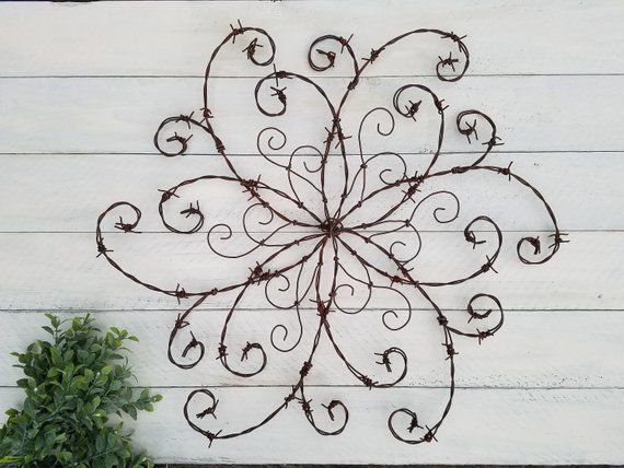 a metal wall hanging on the side of a white building with a plant next to it