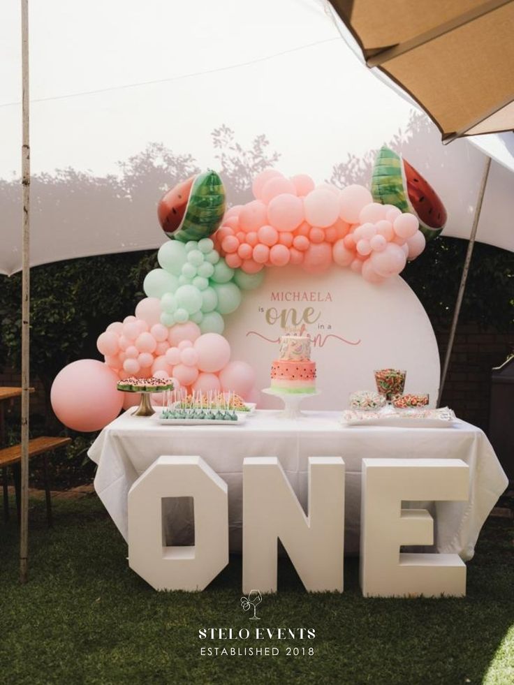 a table topped with lots of balloons and cupcakes on top of a field