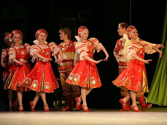 a group of people standing on top of a stage wearing red and gold outfits with head coverings