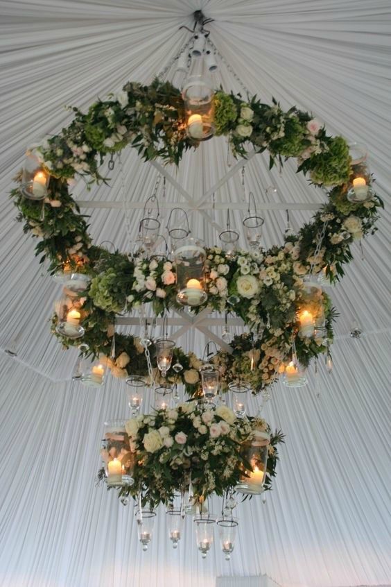 a chandelier with candles and flowers hanging from it's sides in front of a white tent