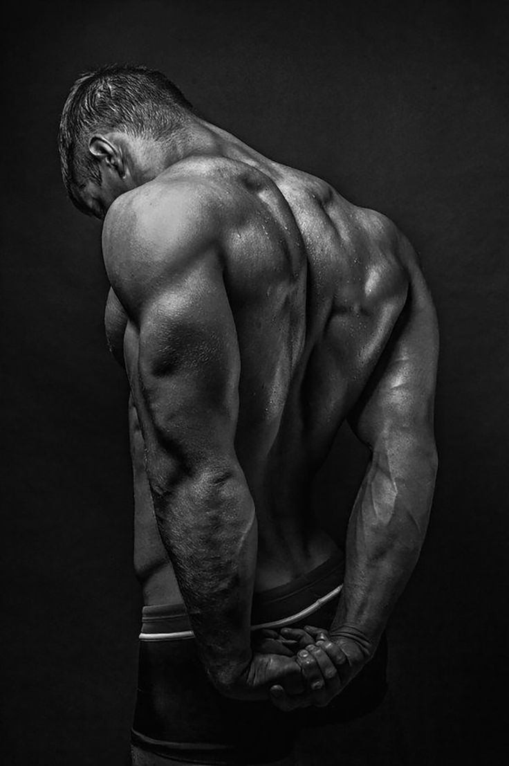 a man with his back turned to the camera, looking down at his shirtless torso