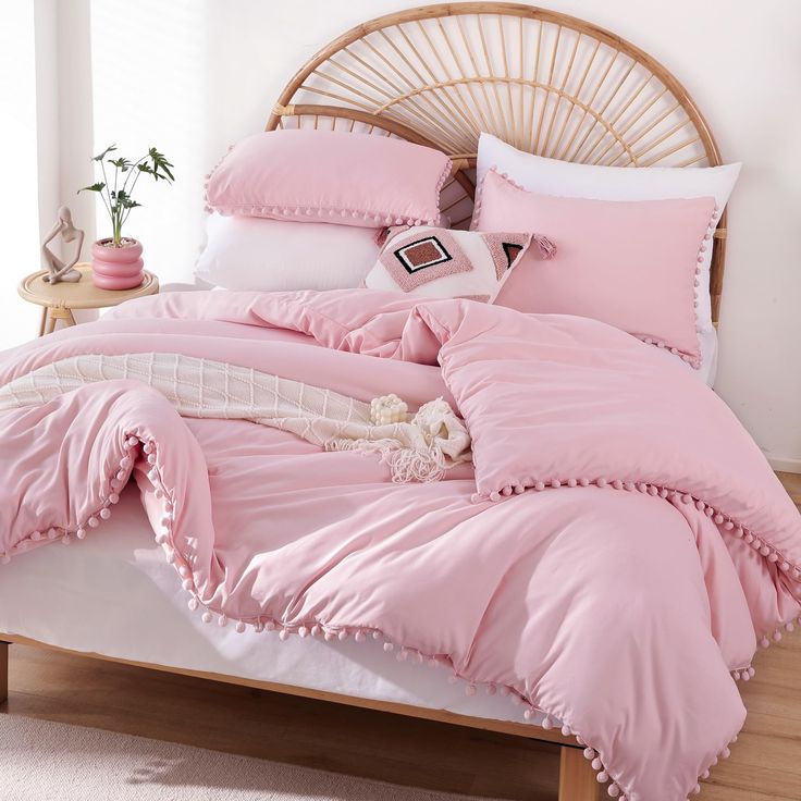 an unmade bed with pink sheets and pom - poms on the pillows