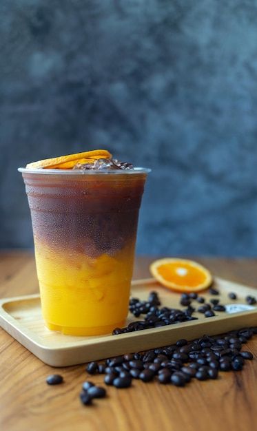 an orange and black drink sitting on top of a wooden table next to coffee beans