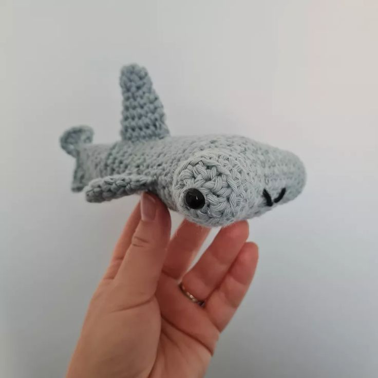 a hand holding a small gray crocheted toy shark