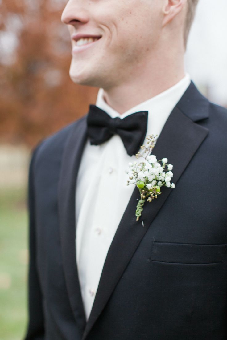 a man in a tuxedo smiles at the camera while wearing a boutonniere