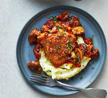 a blue plate topped with mashed potatoes and meat covered in marinara sauce next to a cup of coffee