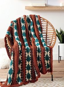 an orange and green blanket sitting on top of a chair next to a potted plant