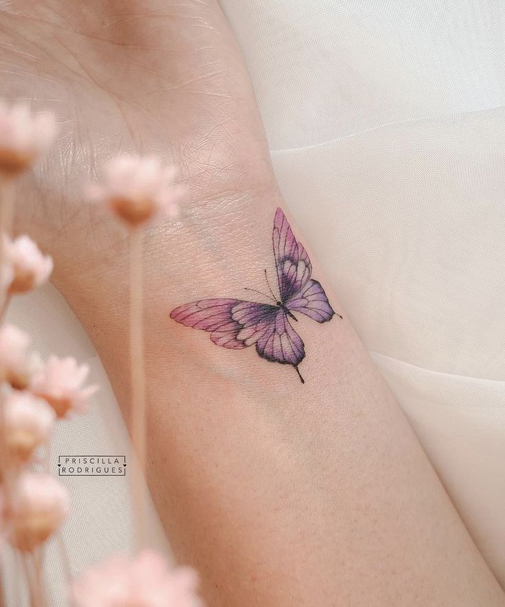 a woman's arm with a small purple butterfly tattoo on the left side of her wrist