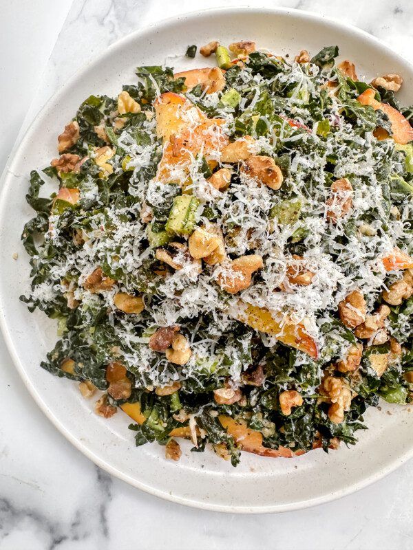 a white plate topped with salad covered in parmesan cheese and nuts on top of a marble table