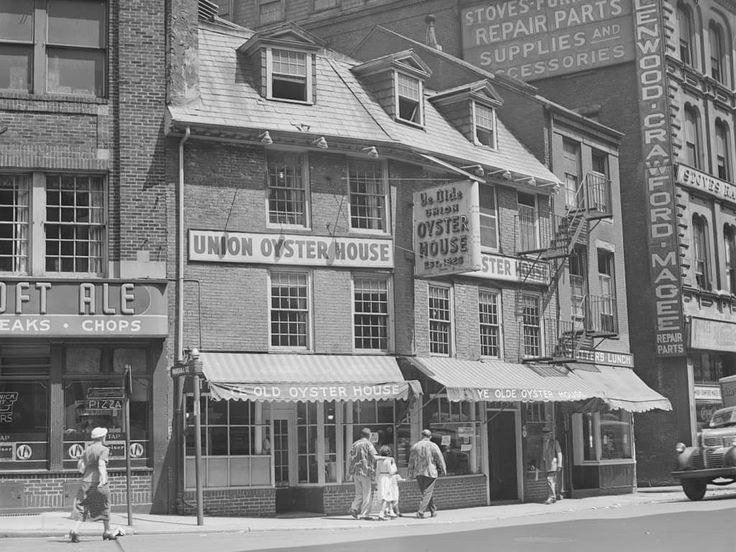 an old black and white photo of people walking on the sidewalk in front of stores