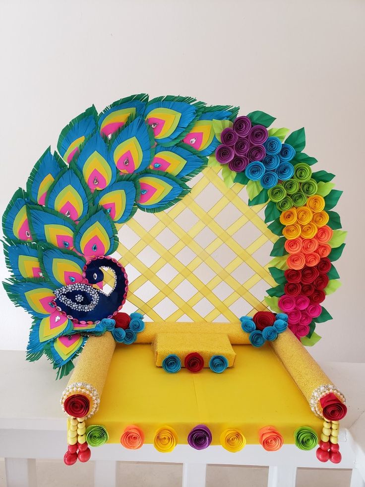 a paper peacock sitting on top of a yellow table next to a decorative piece of art