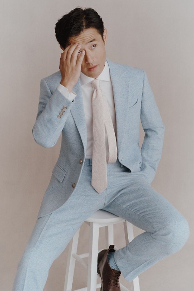 a man in a blue suit sitting on a stool with his hand to his face