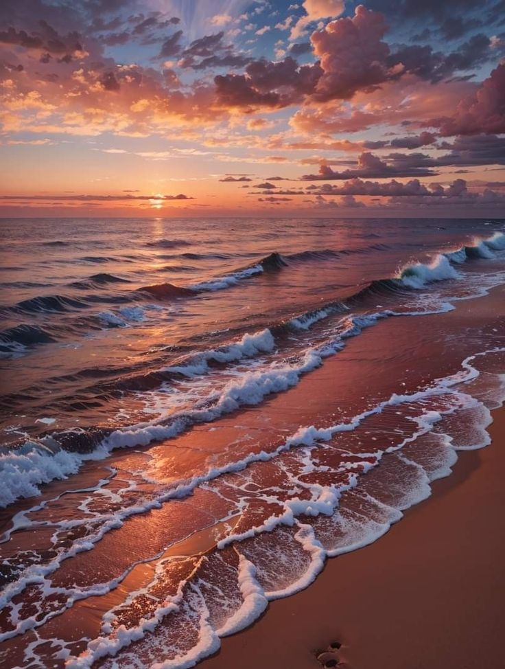 the sun is setting over the ocean with waves coming in and footprints on the sand